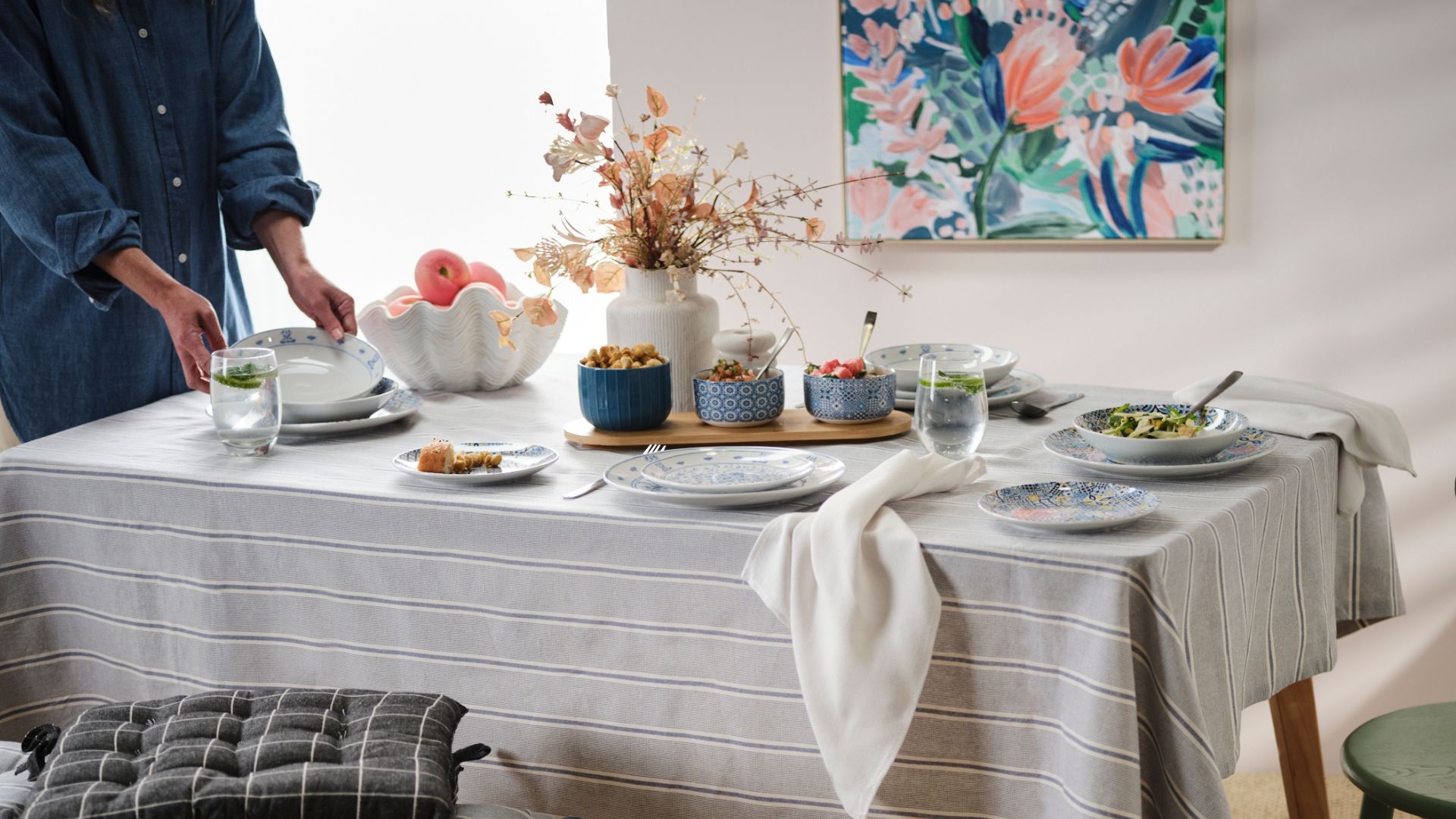 Dining table covered in a striped tablecloth and set with blue dinnerware and shell fruit bowl